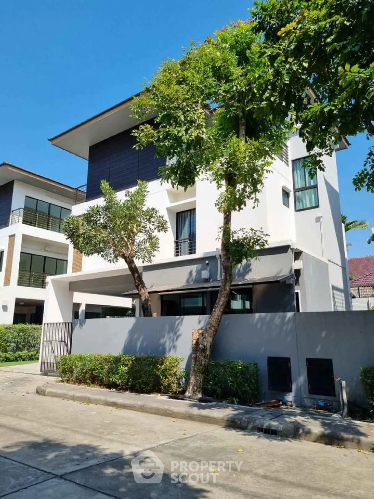 Modern three-story house with sleek design and lush greenery in a serene neighborhood.