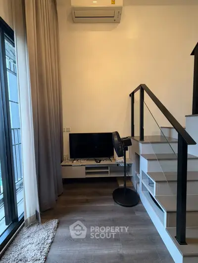 Modern living room with sleek staircase and large window, featuring stylish decor and air conditioning.