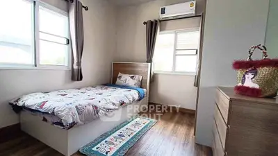 Cozy bedroom with wooden flooring and natural light, featuring a single bed and modern decor.