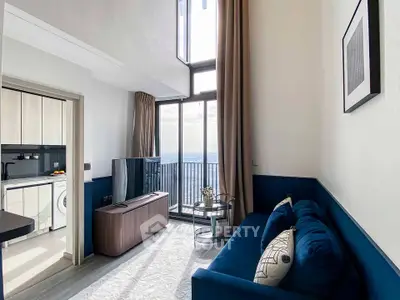 Modern living room with high ceiling and large windows offering stunning city views, adjacent to a sleek kitchen.