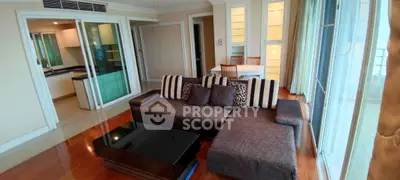 Spacious living room with modern sofa and dining area, featuring large windows and wooden flooring.