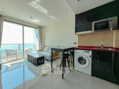 Modern living room with ocean view, featuring sleek kitchen and cozy balcony seating.