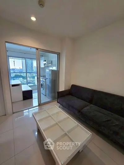Modern living room with sleek black sofa and glass coffee table, overlooking cityscape through large windows.