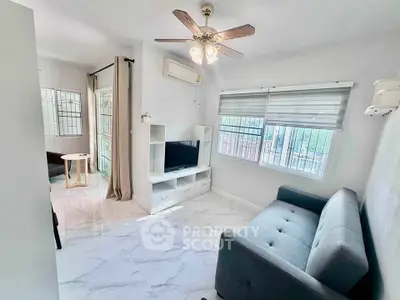 Bright living room with modern sofa, TV, and ceiling fan, featuring large windows and marble flooring.