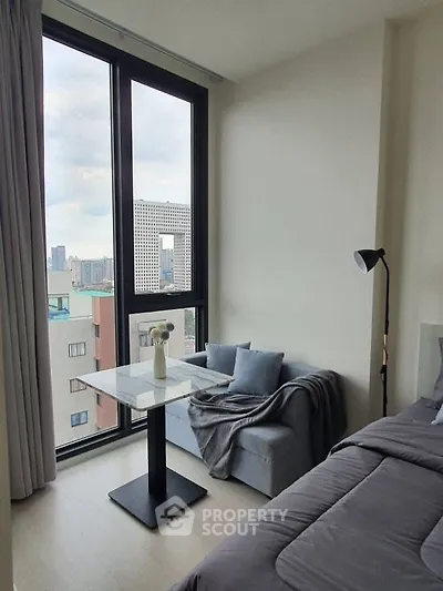 Modern bedroom with city view, featuring cozy seating and stylish decor.