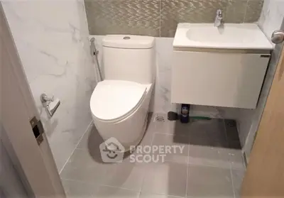 Modern bathroom with sleek toilet and compact sink in a stylish tiled setting.
