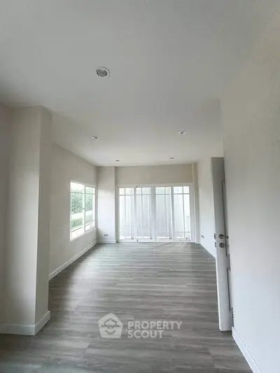 Spacious empty room with large windows and wooden flooring, perfect for customization.