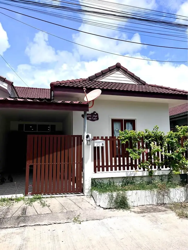 Charming single-story house with red roof and wooden gate under a clear blue sky.