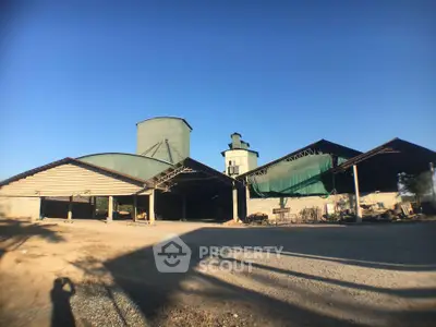 Expansive industrial warehouse with large open spaces and green silos under a clear blue sky.