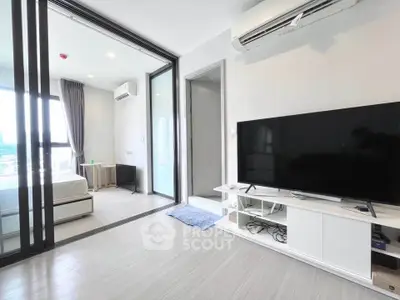 Modern living room with sleek TV setup and air conditioning, adjacent to a bright bedroom with large windows.