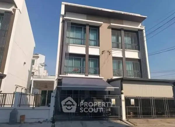Modern three-story townhouse with sleek facade and gated entrance in urban setting.