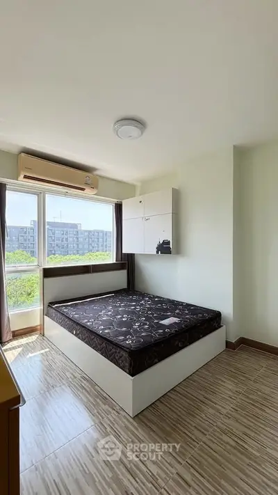 Bright bedroom with large window and modern air conditioning unit, offering a serene view.