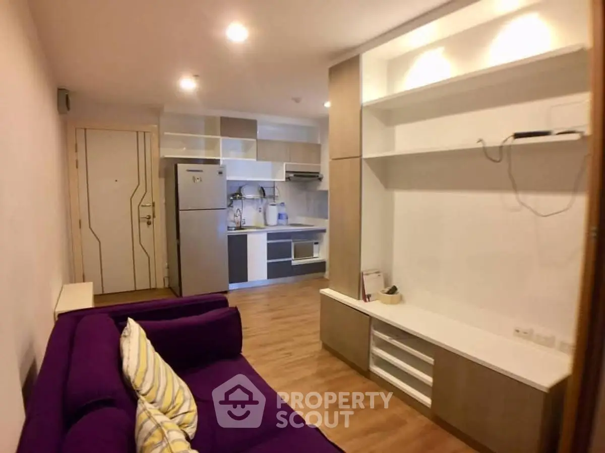 Modern living room with purple sofa and sleek kitchen in open layout apartment.