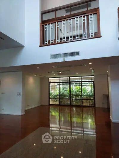 Spacious modern living room with high ceilings and large windows overlooking greenery.