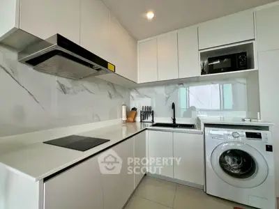 Modern kitchen with sleek white cabinets, marble backsplash, and built-in appliances including washing machine.
