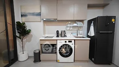 Modern kitchen with sleek appliances including washing machine, microwave, and fridge in stylish apartment.