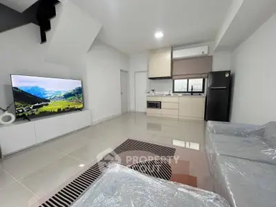 Modern open-plan living room with sleek kitchen and large TV, perfect for contemporary living.