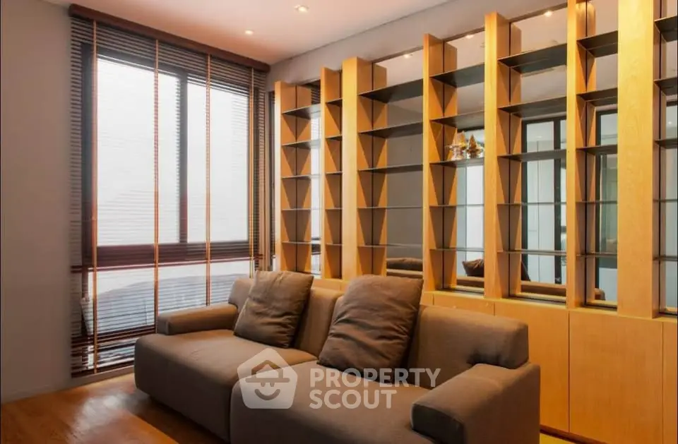 Modern living room with stylish shelving and comfortable sofa, featuring floor-to-ceiling windows for natural light.