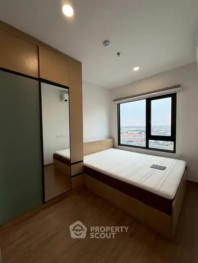 Modern bedroom with large window and city view, featuring sleek wooden flooring and built-in wardrobe.