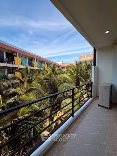 Spacious balcony with lush palm tree views in modern apartment complex.