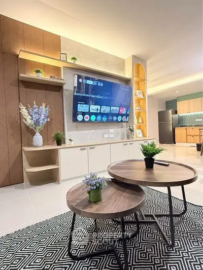 Modern living room with stylish decor and open kitchen layout, featuring a sleek TV setup and elegant furniture.
