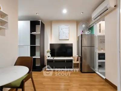 Modern living room with sleek furniture and open kitchen layout, featuring a TV and stainless steel appliances.