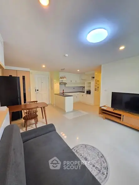 Modern open-layout living room with kitchen, featuring sleek furniture and bright lighting.