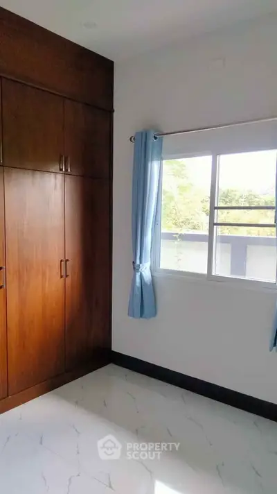 Spacious bedroom with large window and built-in wooden wardrobe