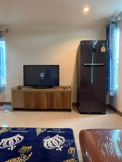 Modern living room with TV and refrigerator, featuring stylish decor and ample natural light.