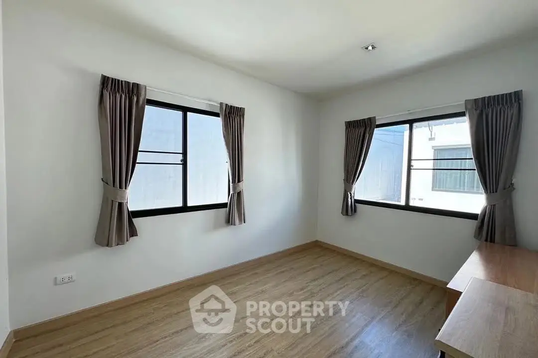 Bright empty room with wooden flooring and large windows, perfect for customization.
