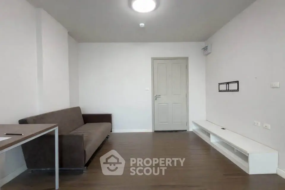 Modern minimalist living room with sleek wooden flooring and neutral tones, featuring a cozy sofa and wall-mounted TV bracket.