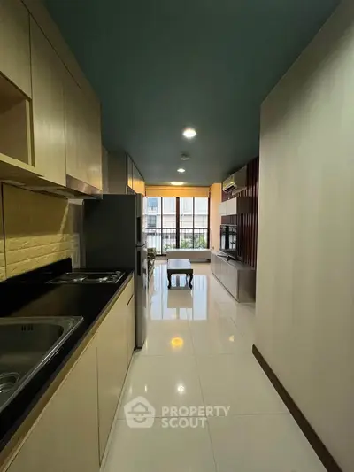 Modern kitchen with sleek cabinetry and open layout leading to a bright living area with large windows.