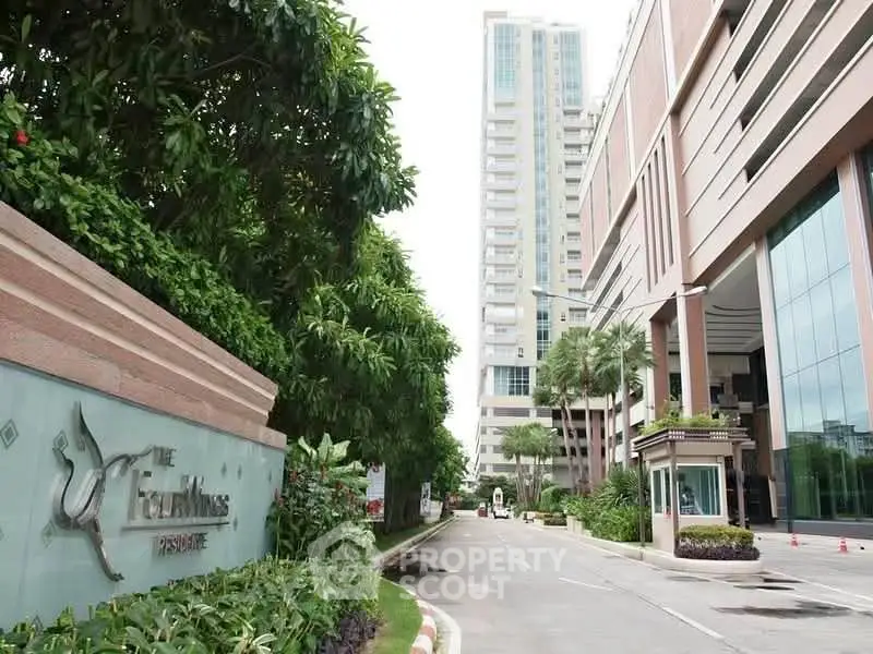 Luxurious high-rise building entrance with lush greenery and modern architecture.