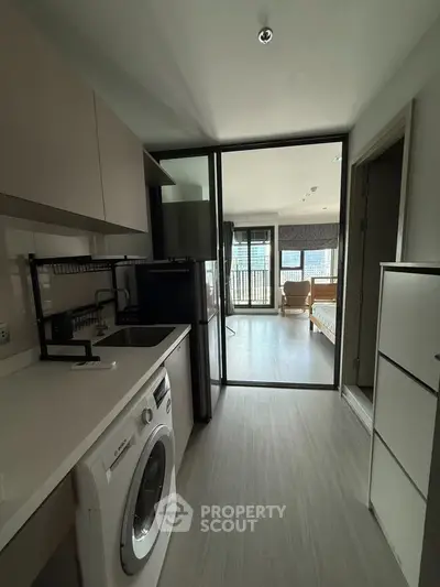 Modern apartment with sleek kitchen and spacious living area, featuring a washing machine and large windows.