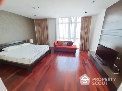 Spacious bedroom with hardwood floors, modern bed, and cozy sofa near large window.