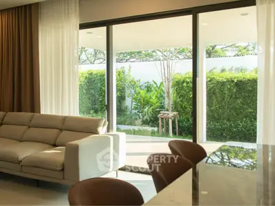 Luxurious living room with large glass doors opening to a lush garden view, featuring elegant furniture and natural light.