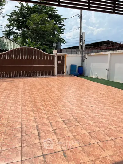 Spacious tiled outdoor area with gated entrance and lush greenery, perfect for gatherings.