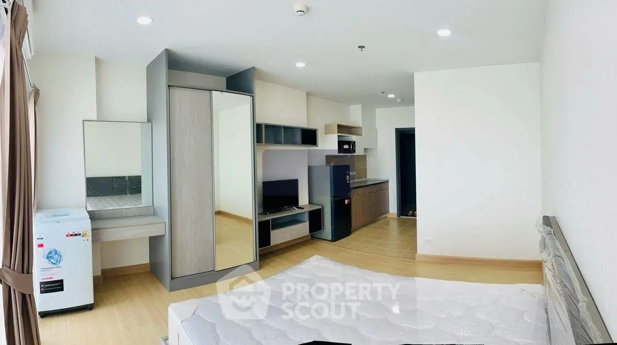 Modern studio apartment with open layout, featuring a compact kitchen and stylish furnishings.