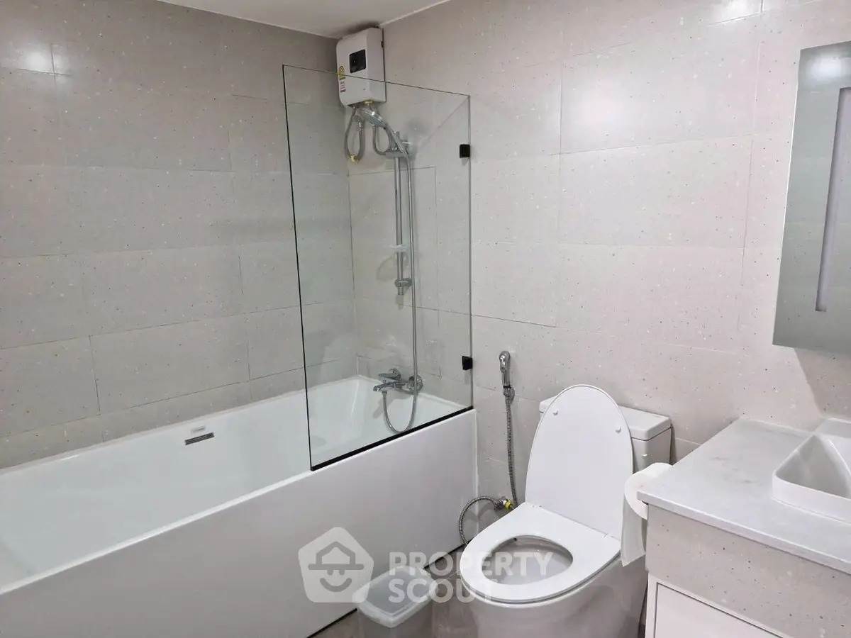 Modern bathroom with sleek design, featuring a glass-enclosed bathtub and contemporary fixtures.