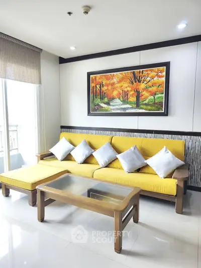 Modern living room with vibrant yellow sofa and scenic artwork, featuring natural light and sleek decor.