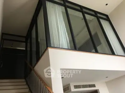 Modern duplex interior with glass walls and staircase, showcasing sleek architectural design.