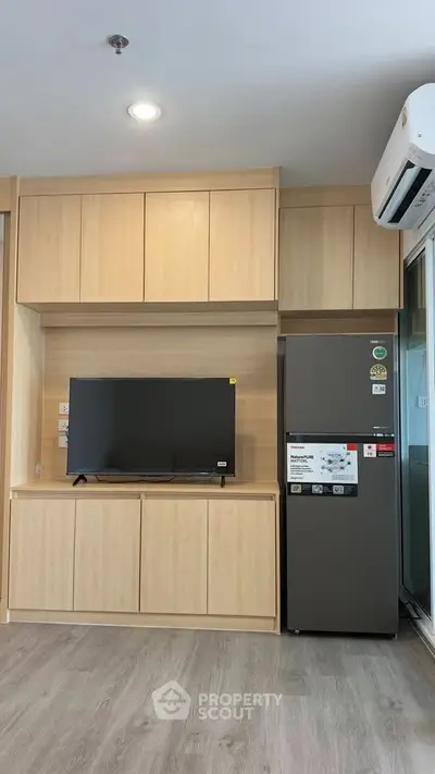 Modern living room with built-in wooden cabinets, flat-screen TV, and sleek refrigerator.