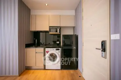 Modern compact kitchen with washing machine, microwave, and fridge in stylish apartment.