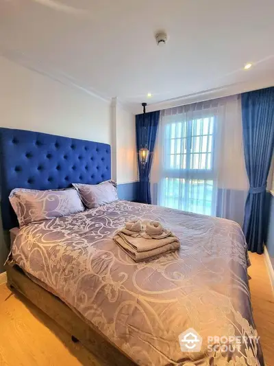 Elegant bedroom with plush blue headboard and natural light through large window.