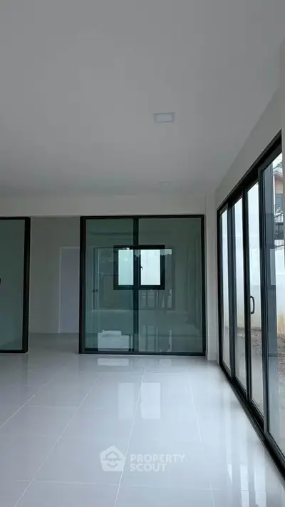 Spacious modern living room with large glass doors and sleek tile flooring.