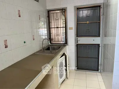 Compact kitchen with tiled walls and stainless steel sink, featuring secure metal doors and windows.