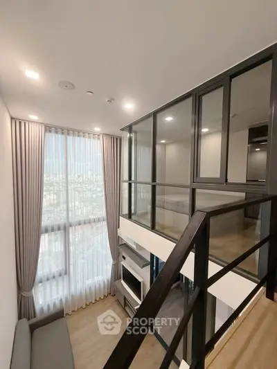 Modern loft-style living room with floor-to-ceiling windows and mezzanine in urban apartment.