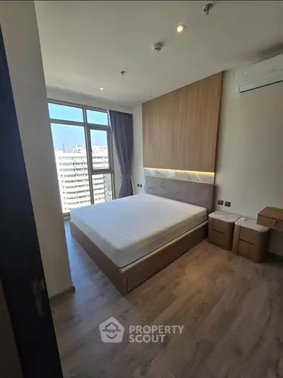 Modern bedroom with large window and city view, featuring sleek wooden furniture and minimalist design.