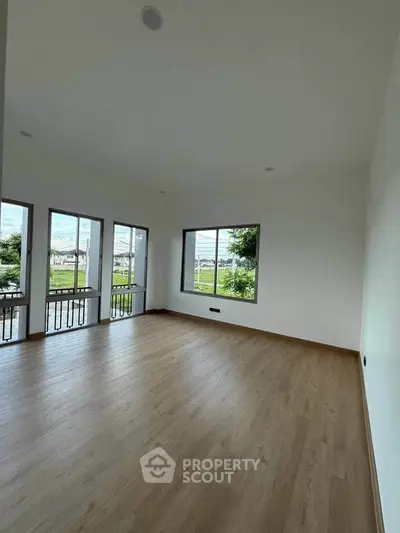 Spacious empty room with large windows and wooden flooring, offering abundant natural light and serene views.