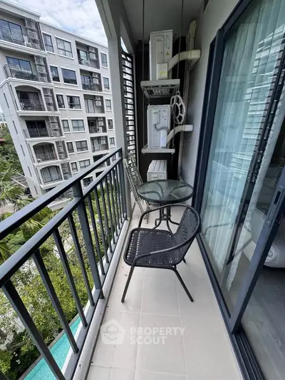 Charming balcony with seating overlooking modern apartment complex and lush greenery.